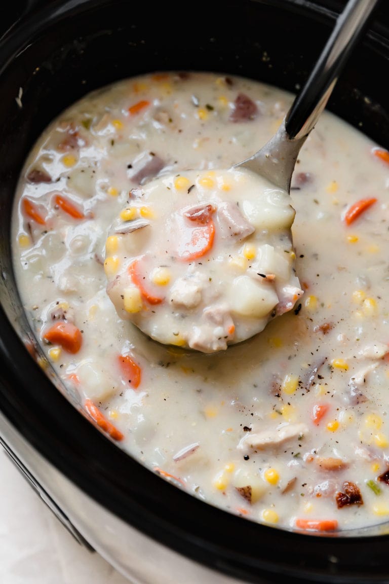 Close up view of slow cooker chicken corn chowder being scooped with a soup ladle. 