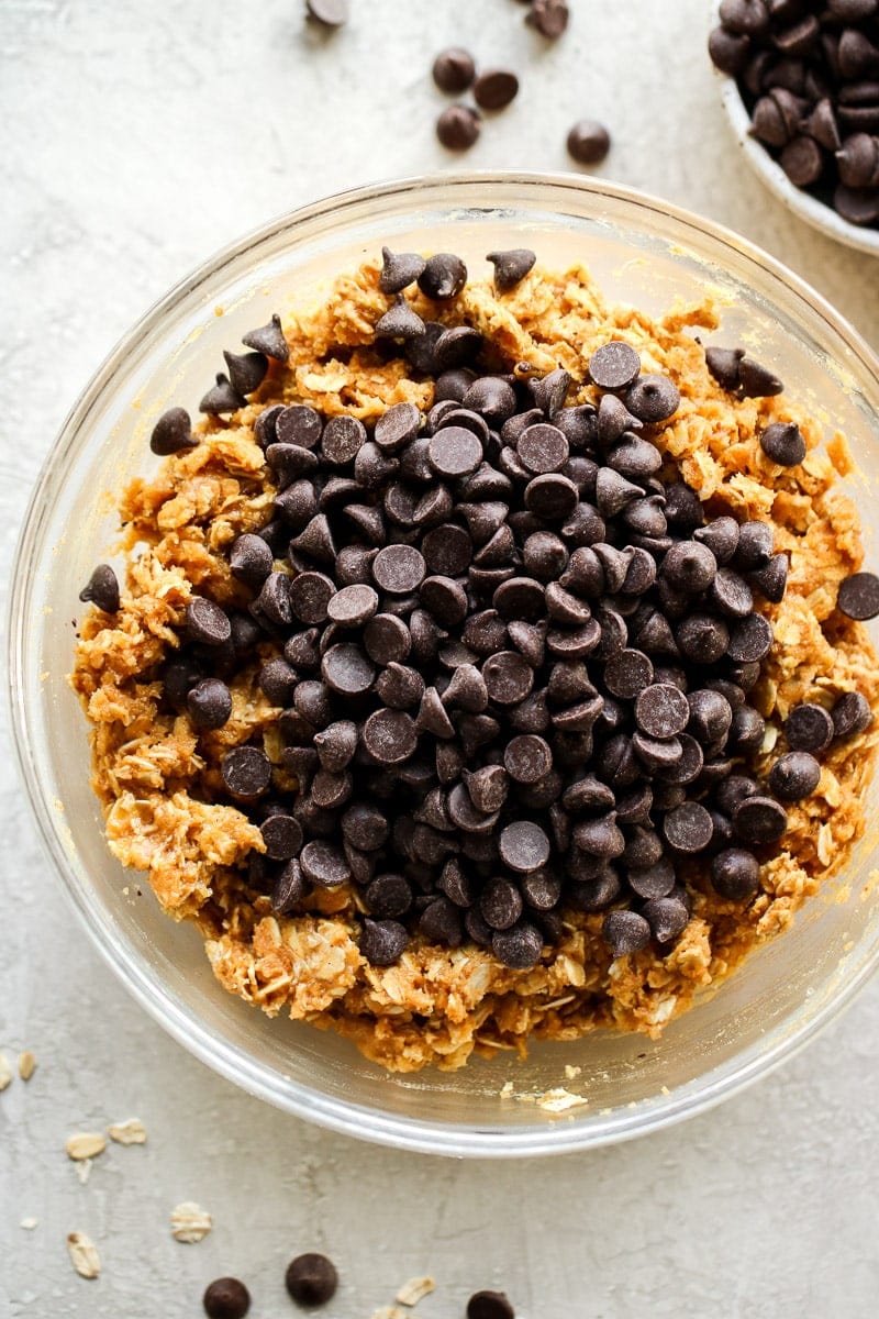Chocolate chips added on top of peanut butter oatmeal cookie dough ready to be mixed in