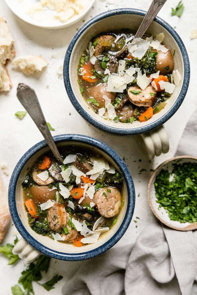 Two bowls with handles filled with Harvest Italian soup with sausage and potatoes. Topped with shaved Parmesan.