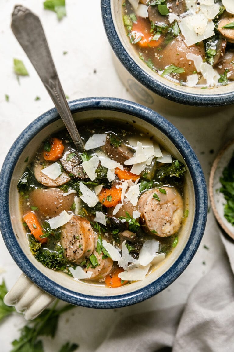Overhead view of two cups of Italian soup with sausage topped with shaved parmesan cheese. 
