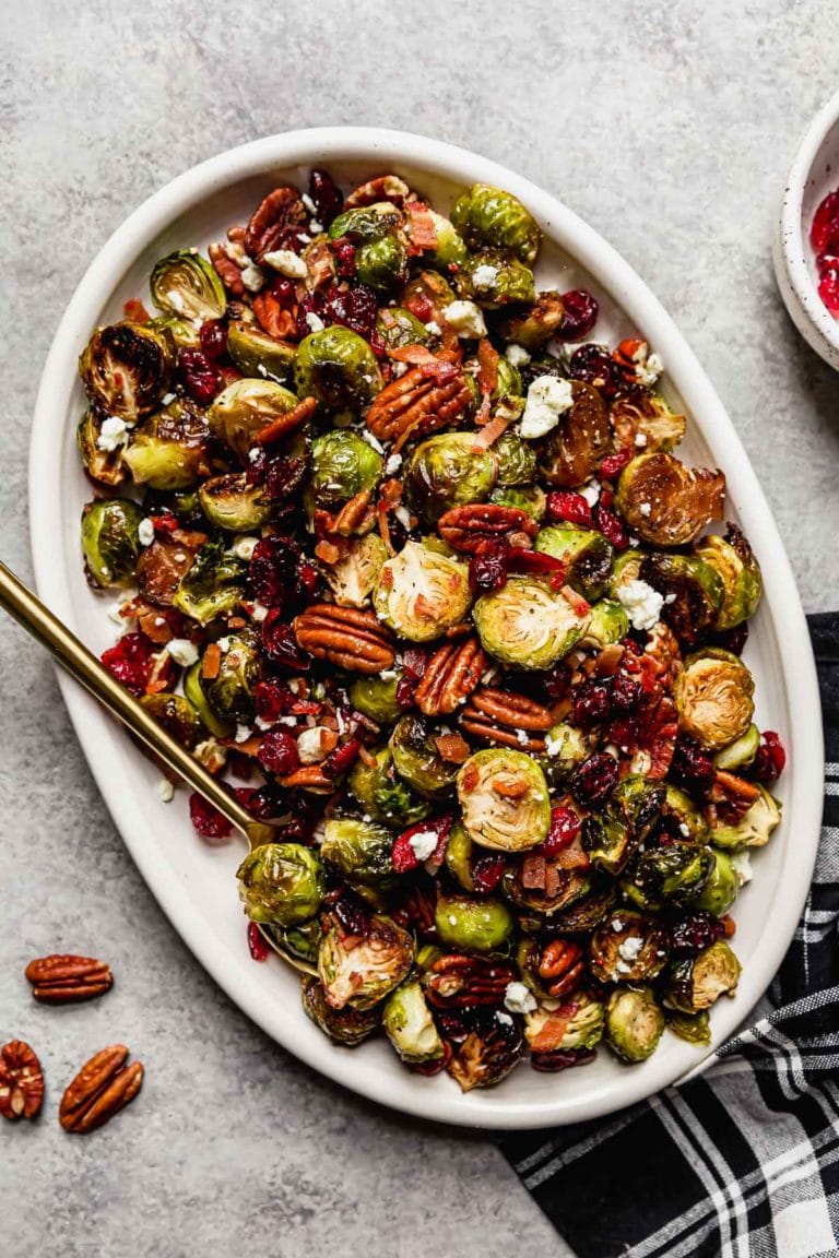 Overhead view Roasted Brussels sprouts with pecans, cranberries and feta cheese crumbles on a white serving tray.