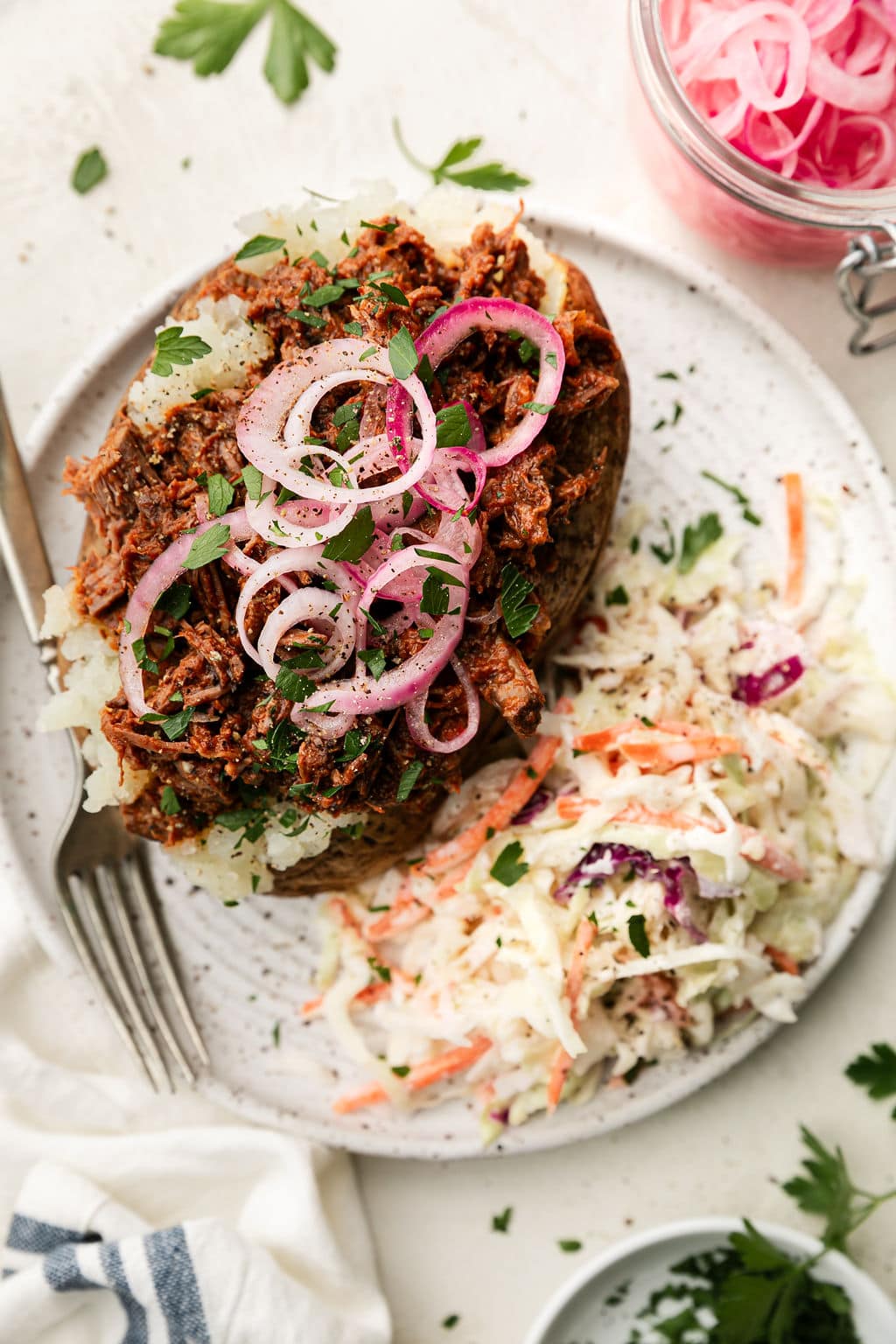 Overhead view baked potato stuffed with shredded BBQ Beef topped with pickled onions with coleslaw on the side