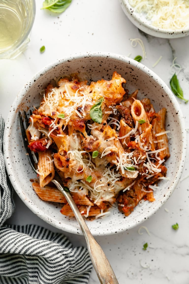 White bowl filled with baked ziti topped with cheese.