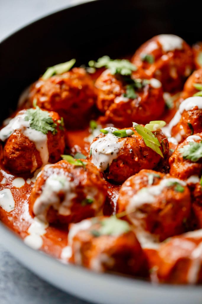 Buffalo Chicken Meatballs in a cast iron skillet drizzled with ranch and topped with green onion and cilantro.