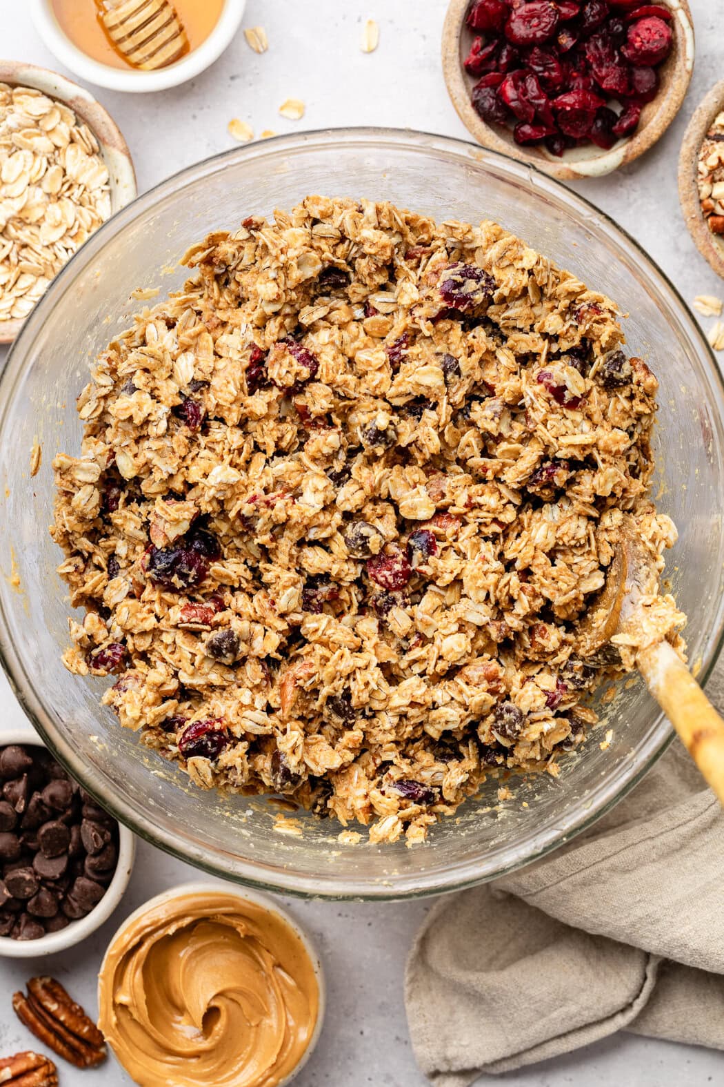 Overhead view of a glass bowl filled with Trail Mix Granola Bar batter with dried cranberries and creamy peanut butter on the side. 