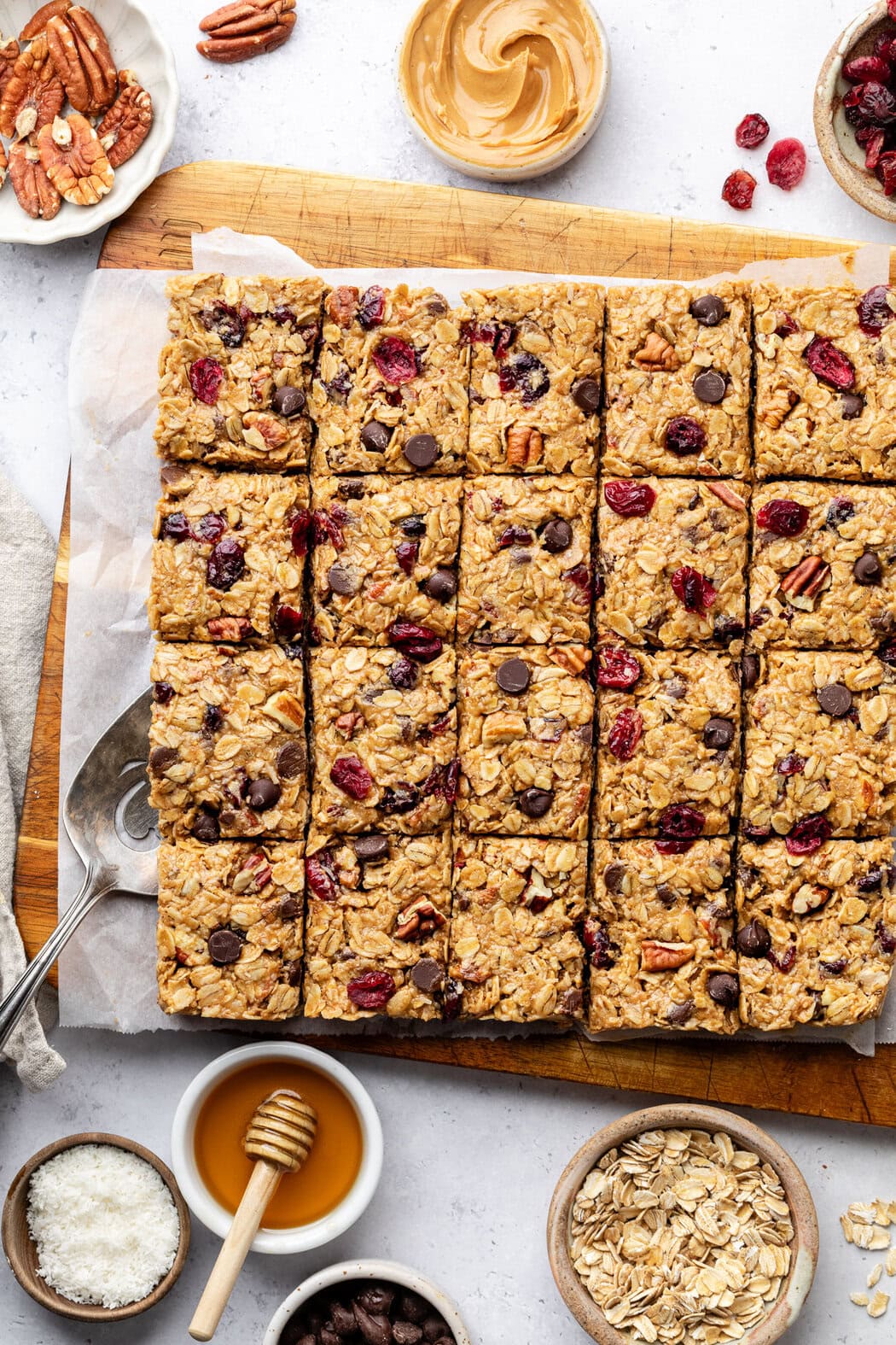 Close up view of a batch of No Bake Trail Mix Granola Bars on a wooden cutting board showing chocolate chip and cranberry pieces. 