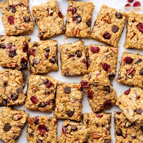 Overhead view of a batch of trail mix bars cut into squares showing pieces of chocolate, nuts, and dried cranberries.