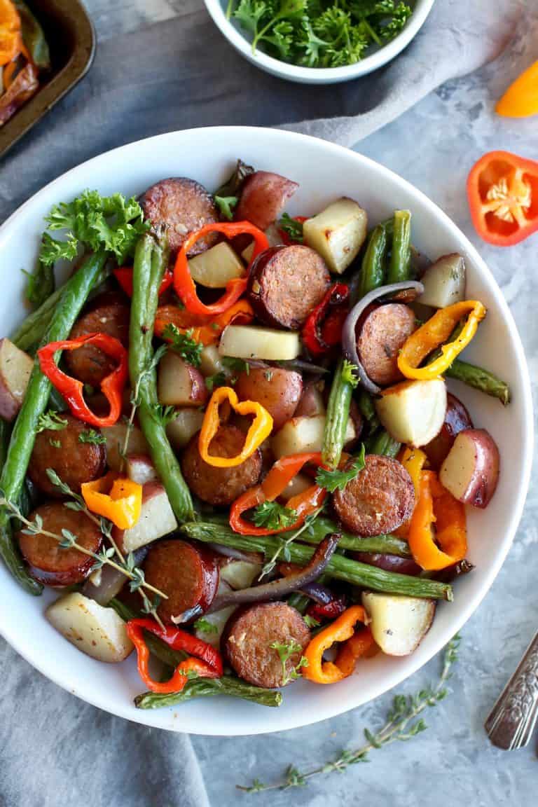 Overhead view of a bowl of sliced pork kielbasa with potatoes and colorful peppers. 