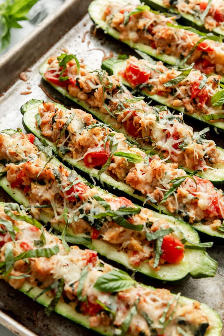 Close up view of a pan of freshly baked Italian stuffed zucchini boats topped with melted cheese and fresh basil. 