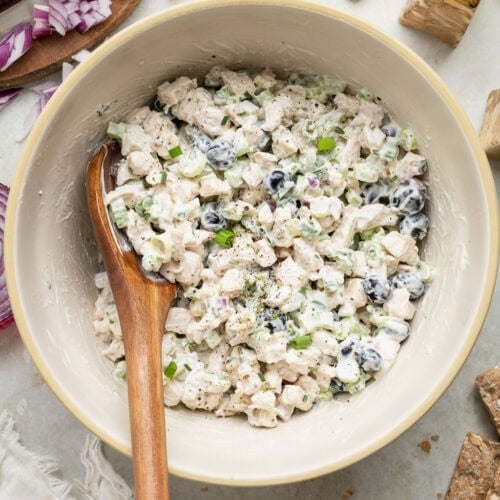 Overhead view of a white bowl filled with fresh blueberry chicken salad with a wooden spoon stuck into the mixture.