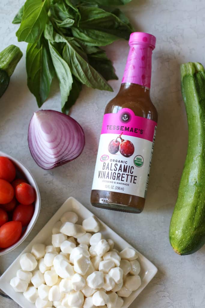 Overhead view of a dressing bottle next to Caprese Zucchini Salad with Balsamic Vinaigrette ingredients