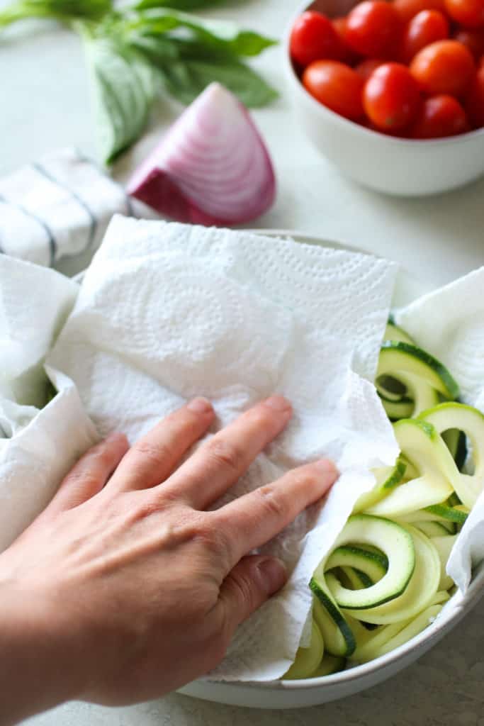 A hand dabbing liquid off zucchini noodles
