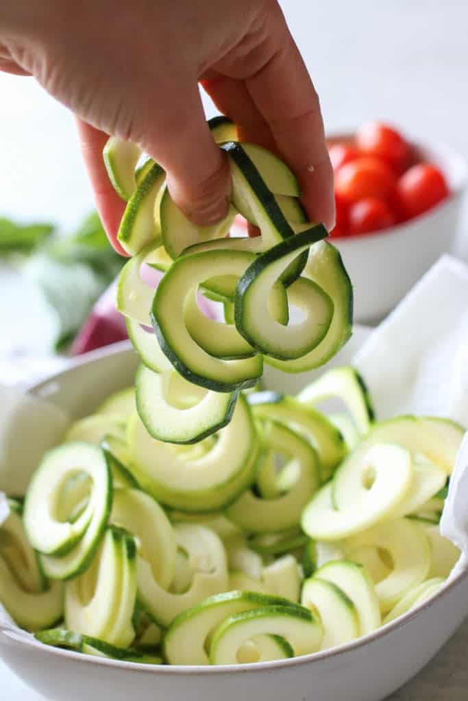 A hand holding a handful of zucchini noodles over a bowl of them