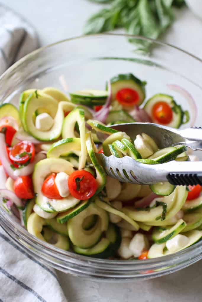 Overhead view of a tongs in a bowl of Caprese Zucchini Salad with Balsamic Vinaigrette