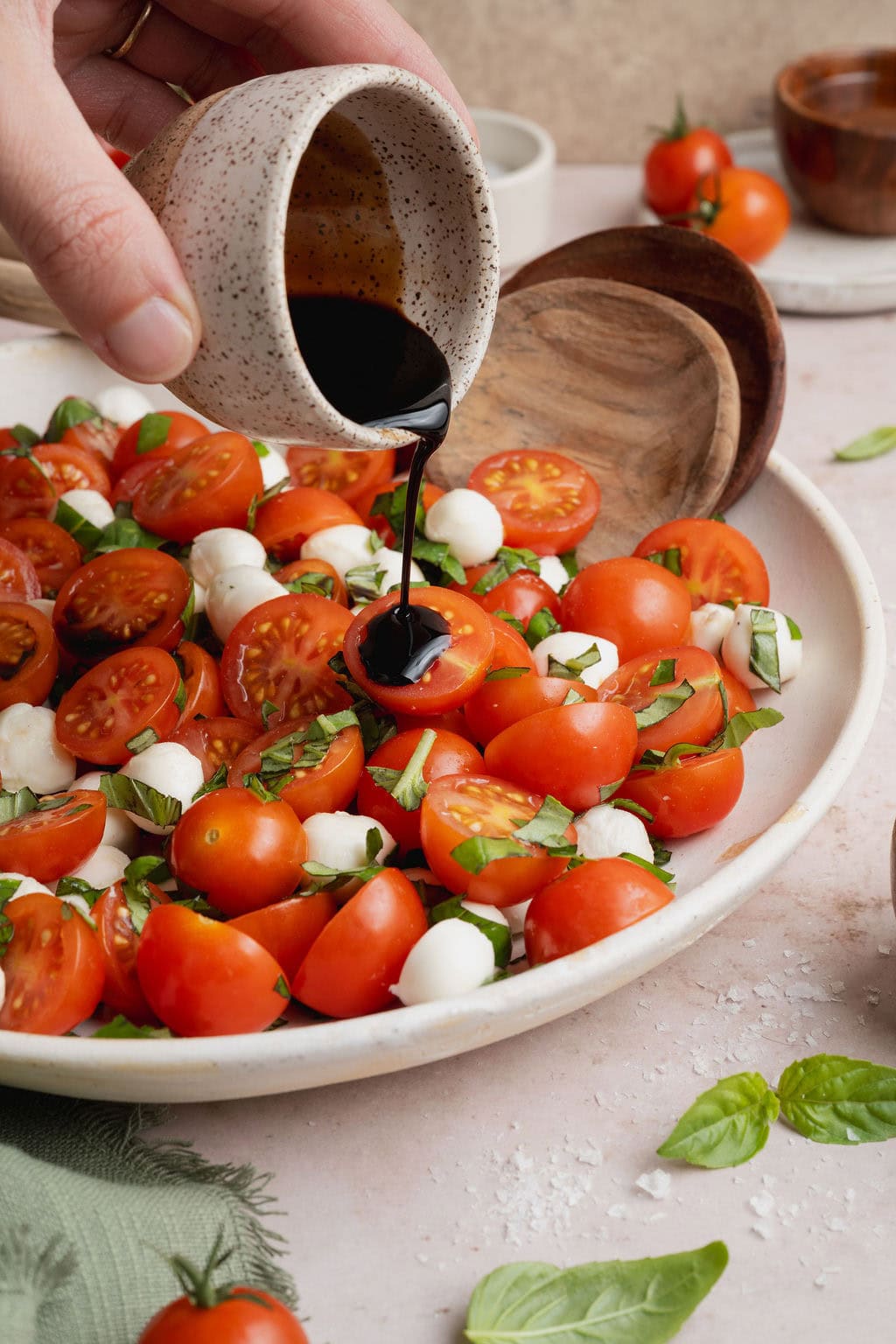 A hand drizzling balsamic glaze over a plate of caprese salad.
