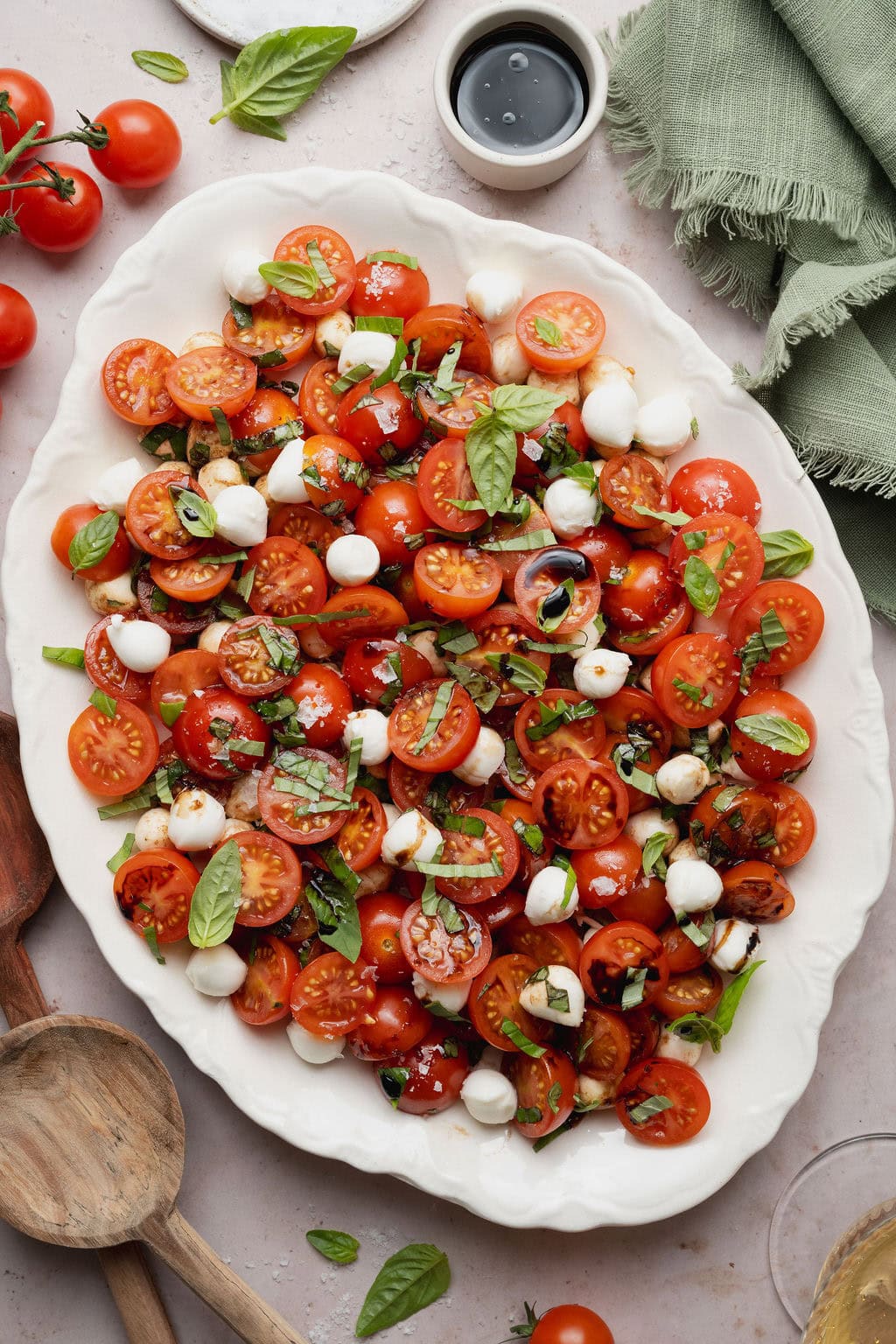A white serving platter topped with a caprese salad finished with a drizzle of balsamic and fresh herbs. 