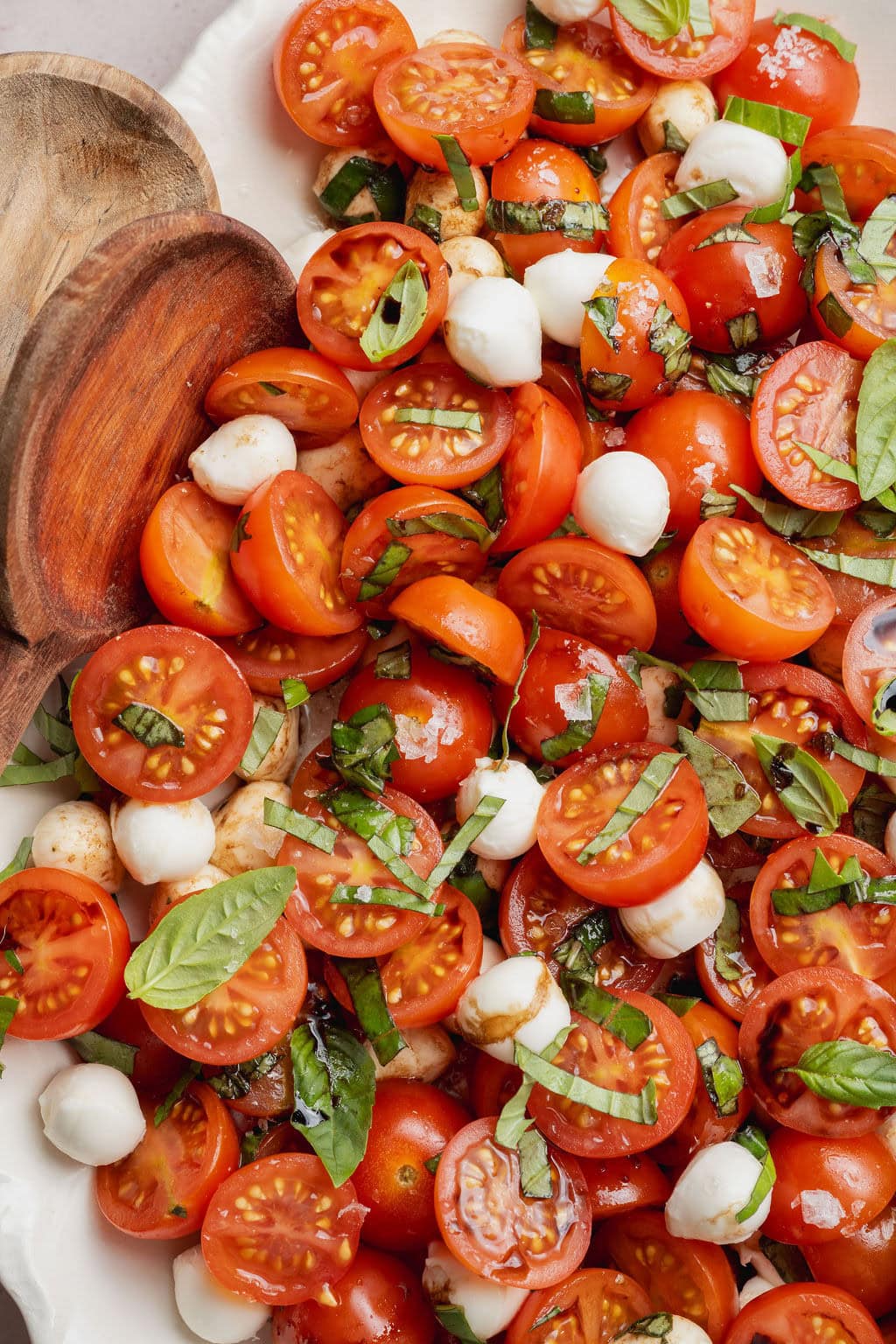 A caprese salad topped with a drizzle of balsamic vinegar, two wooden serving spoons on the side.