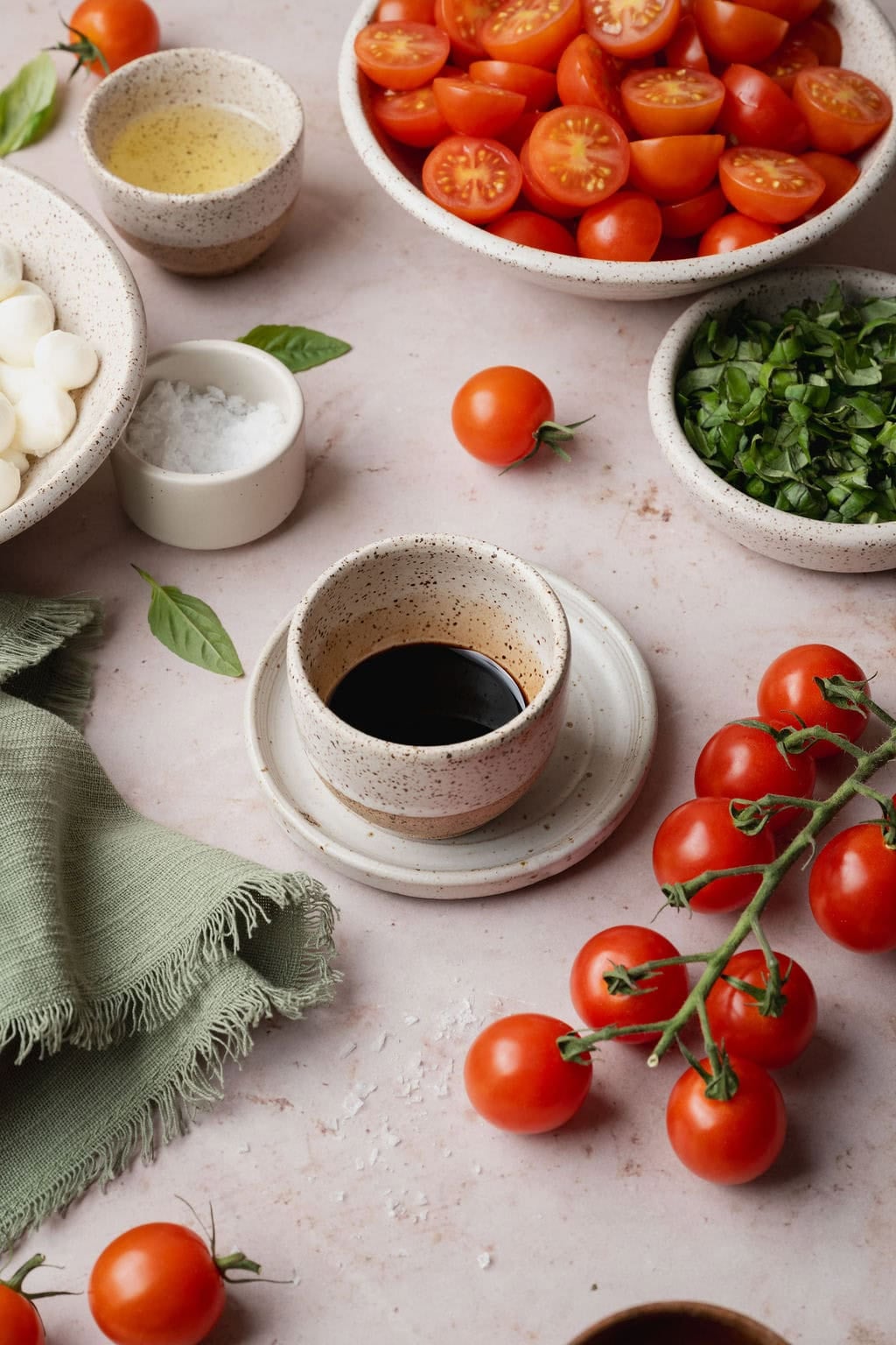 Balsamic glaze cooling in a small bowl surrounded by caprese salad ingredients.