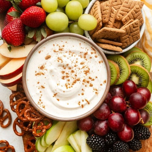 Overhead view of a platter of fresh fruit with a bowl of creamy fruit dip in the middle sprinkled with cinnamon.