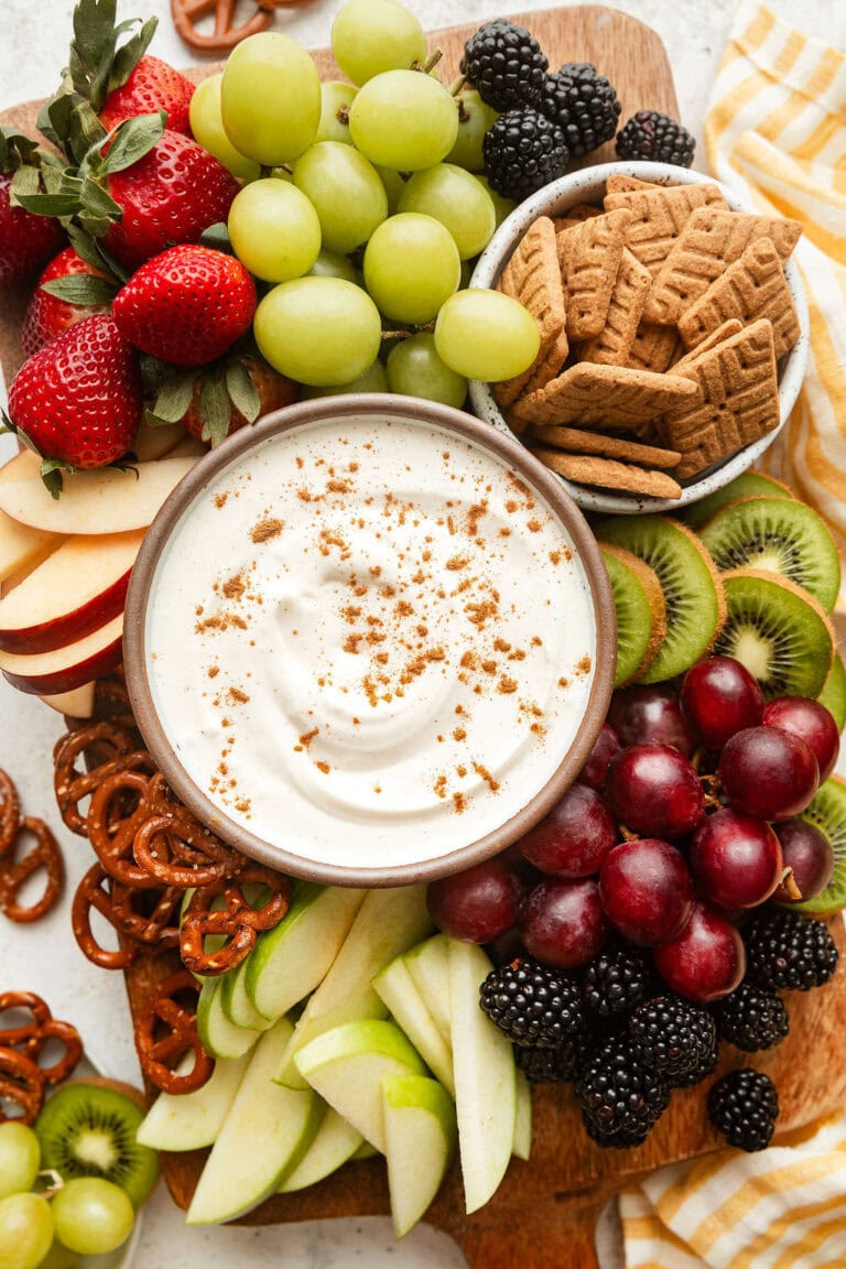 Overhead view of a platter filled with fruit and crackers with a creamy dip in the middle.