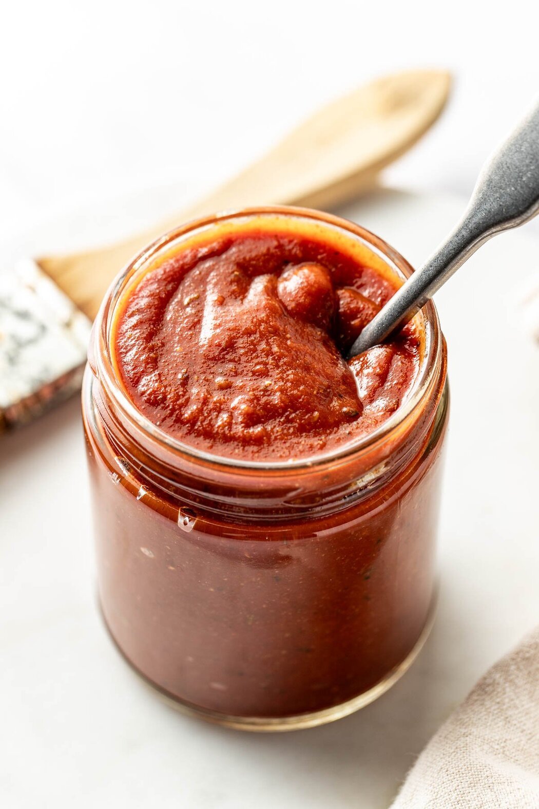 Close up view of a glass jar of Homemade BBQ Sauce with a spoon stuck in the jar.