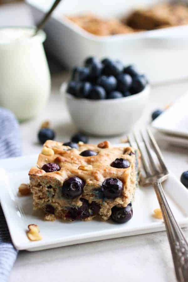 Blueberry Banana Walnut Muffin Bar on a white plate with a fork on the side and a bowl of blueberries in the distance