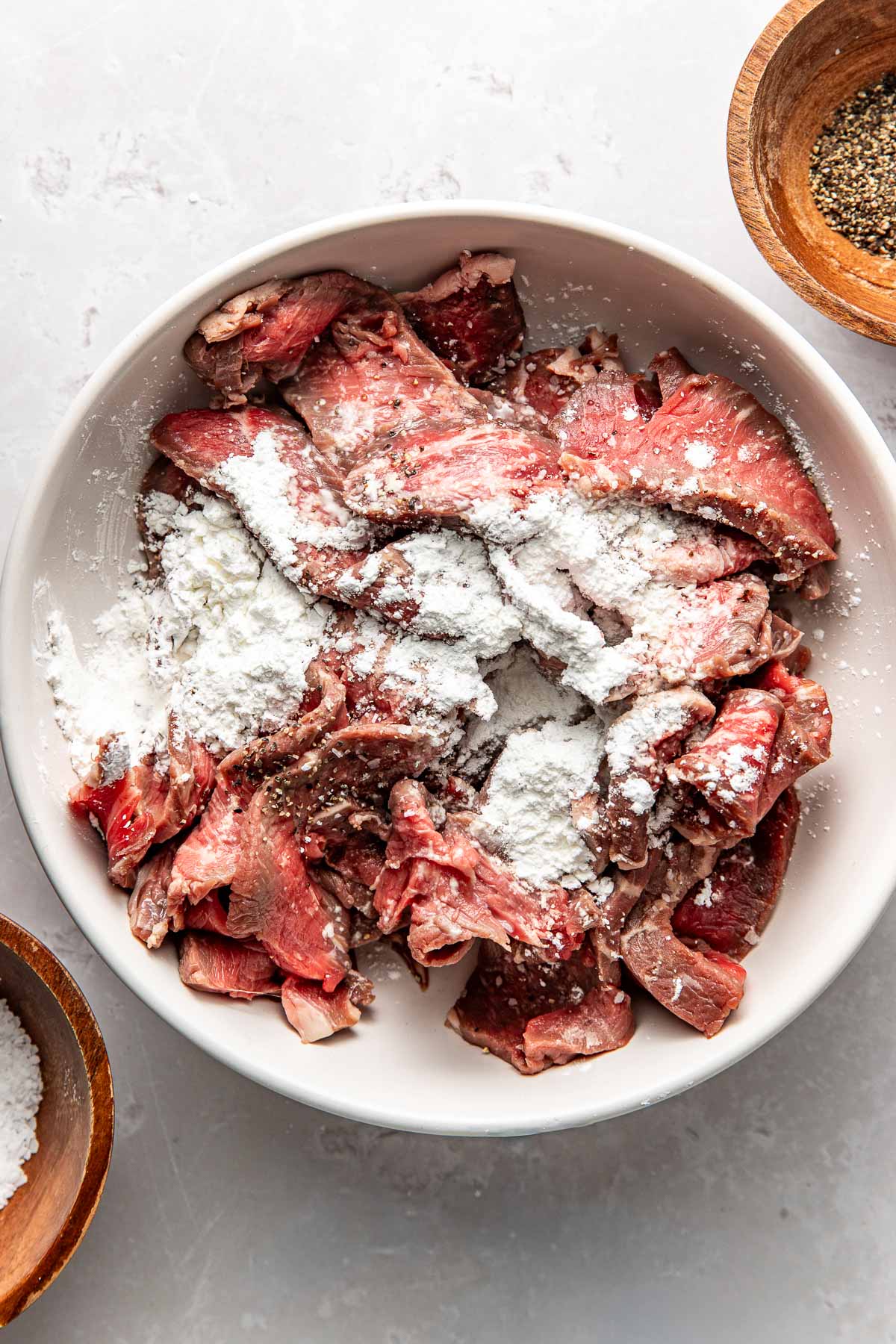 Overhead view of a bowl of thinly sliced raw steak topped with corn starch.