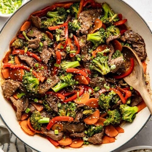 Overhead view of a plate of steak stir fry over white rice and sprinkled with sesame seeds and green onions.