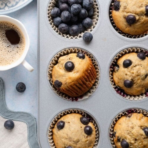 Overhead view of banana blueberry muffins in a muffin pan with a cup of coffee on the side.