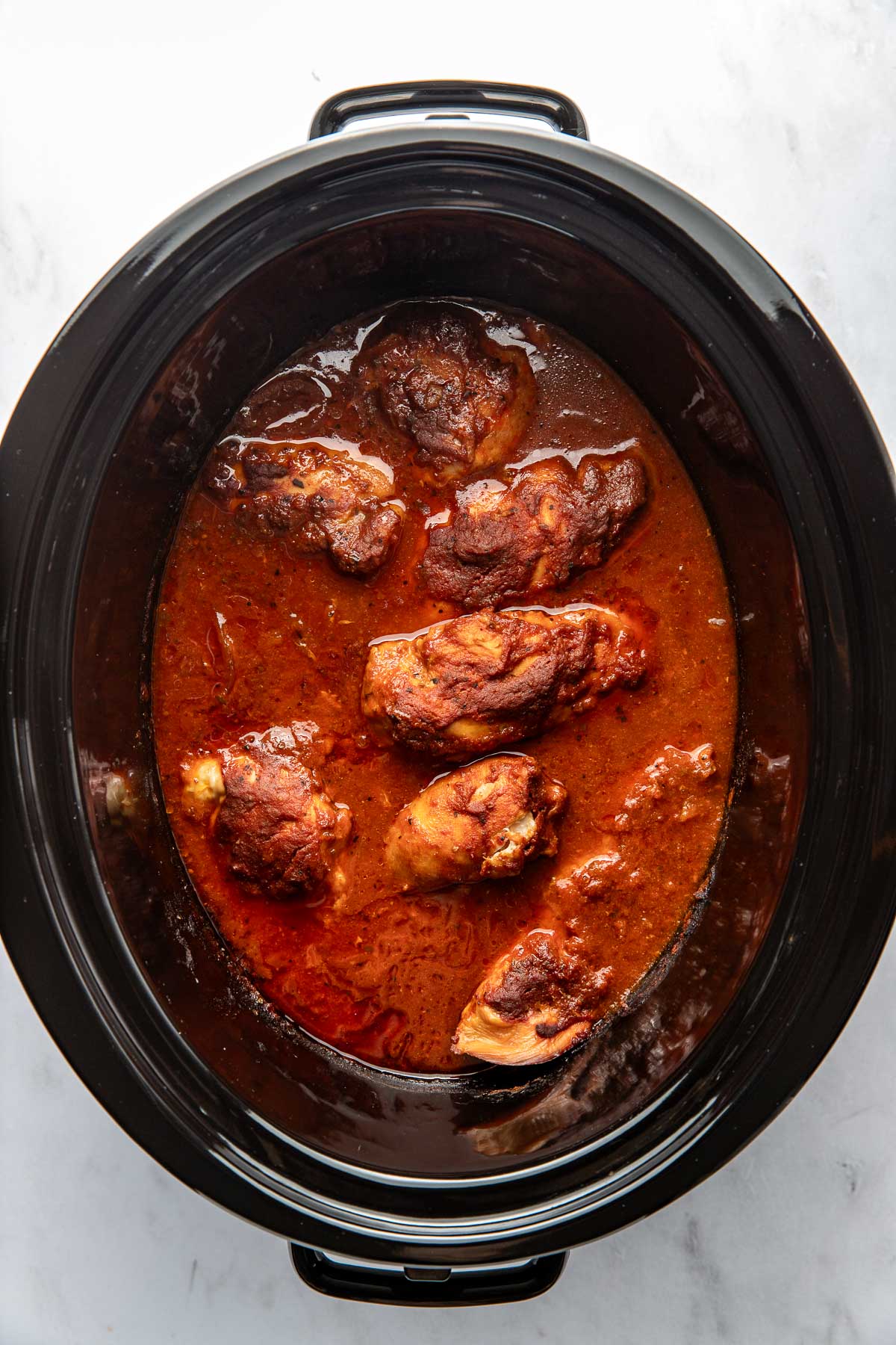 Overhead view of a slow cooker filled with cooked chicken breasts in a BBQ sauce mixture.