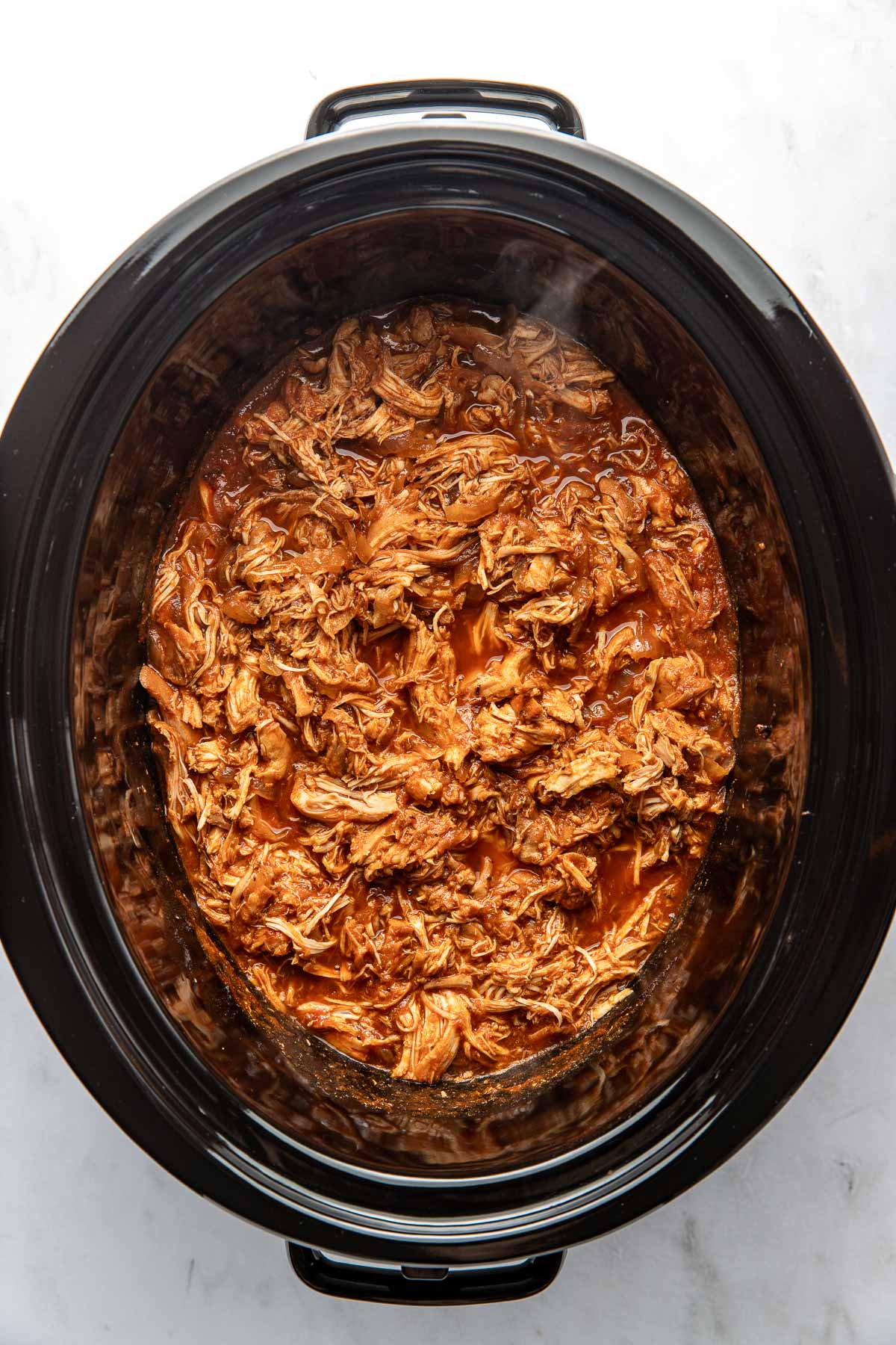 Overhead view of a slow cooker filled with BBQ Pulled Chicken ready for serving.