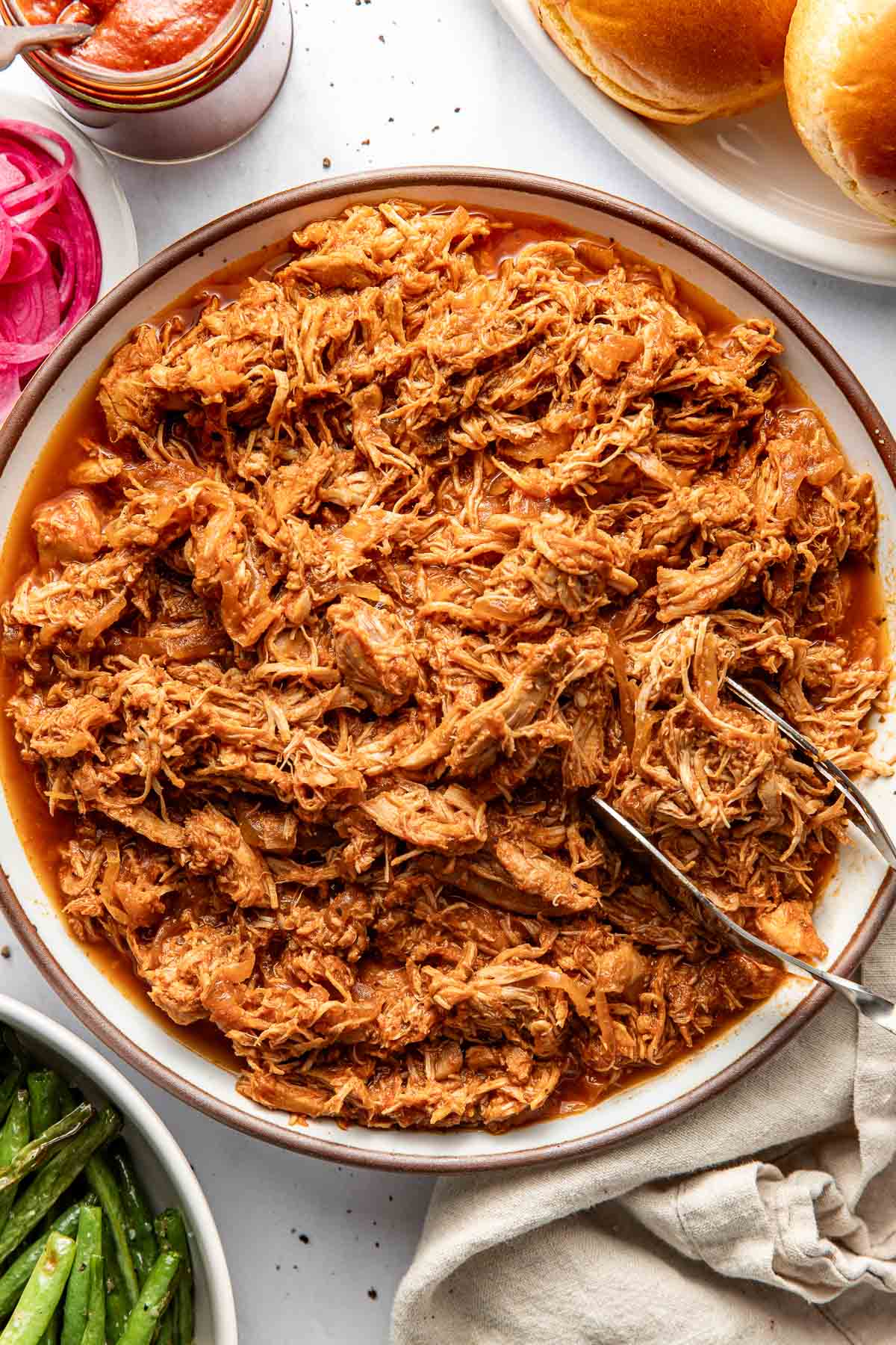 Overhead view of a bowl of BBQ Pulled Chicken with a tong on the side for serving.