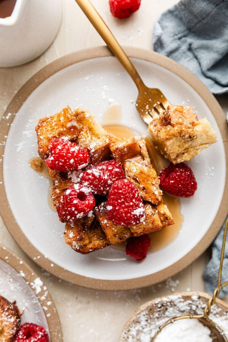 Overhead view of a plate filled with a large piece of French toast casserole topped with red raspberries and sprinkled with powdered sugar.