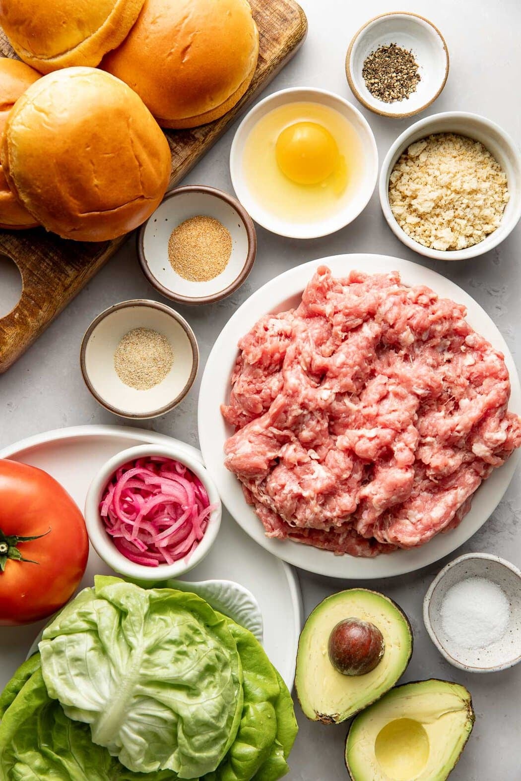 Overhead view of a variety of ingredients for turkey burgers in different sized bowls on a marble countertop. 
