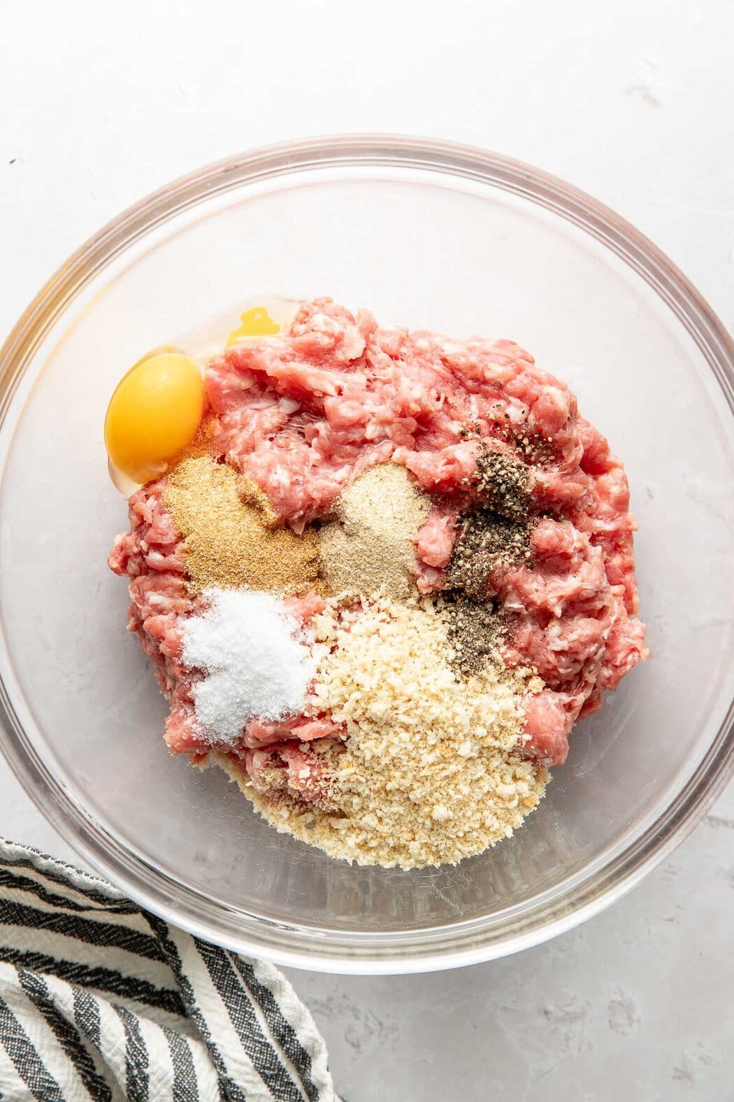 Overhead view of a glass mixing bowl filled with turkey burger ingredients ready for mixing. 