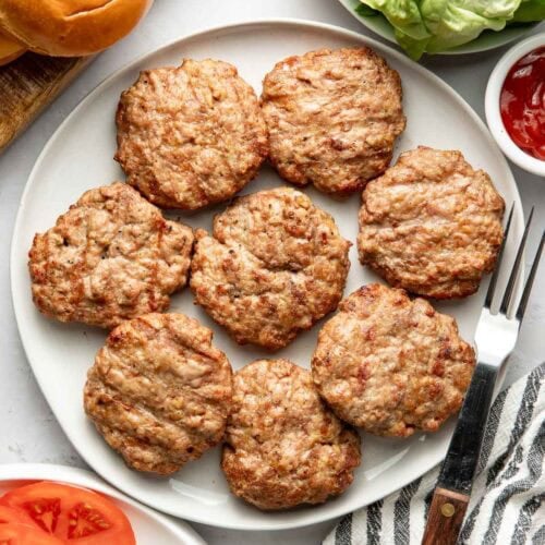 Overhead view of a white platter filled with freshly grilled turkey burger patties.