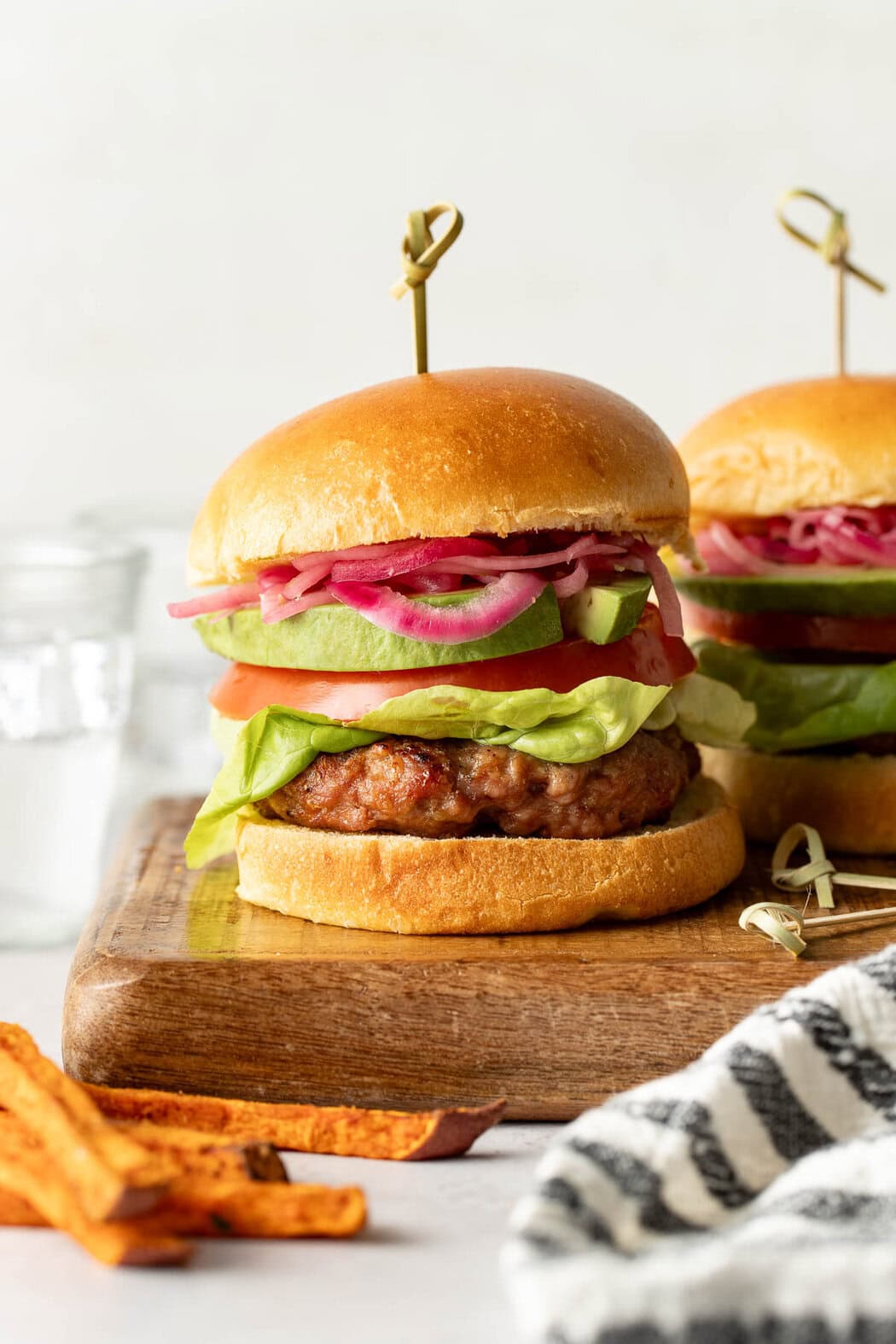 Close up view of two turkey burgers on buns sitting on a wooden cutting board showing all the toppings inside like, red onions, tomato, and lettuce. 