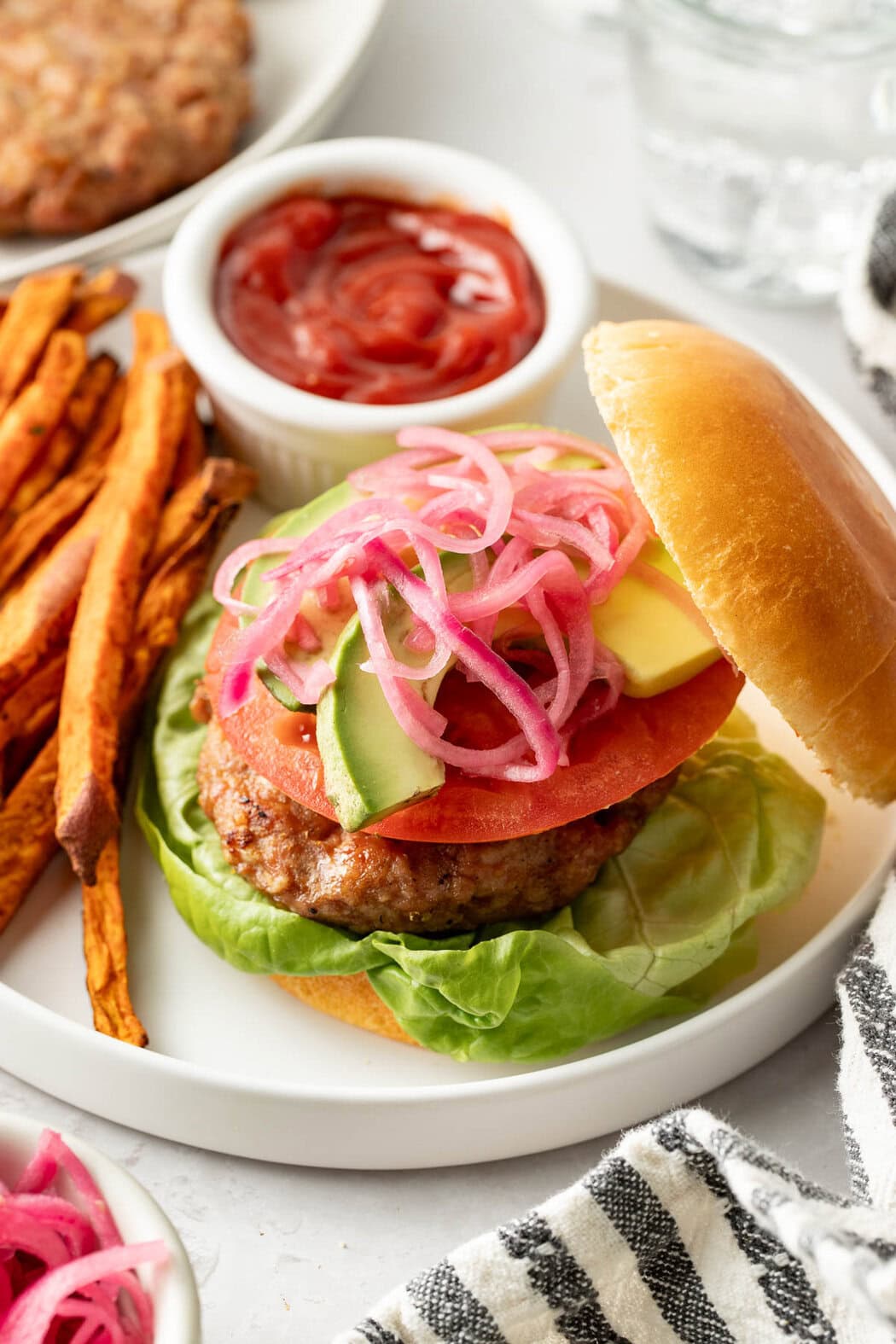 Overhead view of a turkey burger on a bun arranged on a plate with sweet potato fries on the side. 