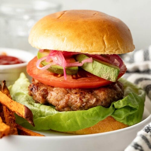 Close up view of a turkey burger on a bun with all the colorful toppings inside like tomato, pickled onions, and fresh lettuce.