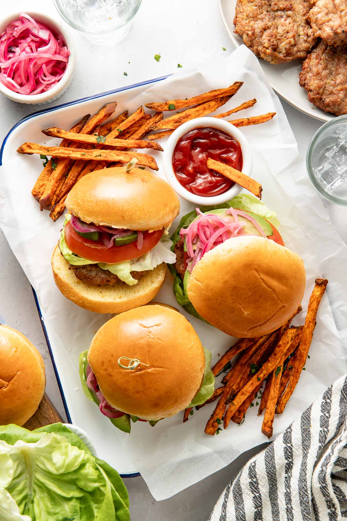 Overhead view of several turkey burgers on buns arranged around fresh sweet potato fries and ketchup on the side. 