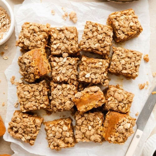 Overhead view of a batch of freshly baked Pumpkin Pie Bars cut into squares on parchment paper.