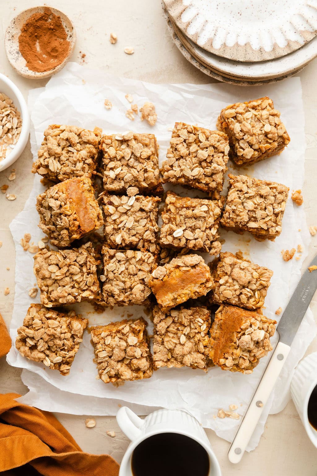 Overhead view of a freshly baked batch of pumpkin pie bars cut into squares on parchment paper. 