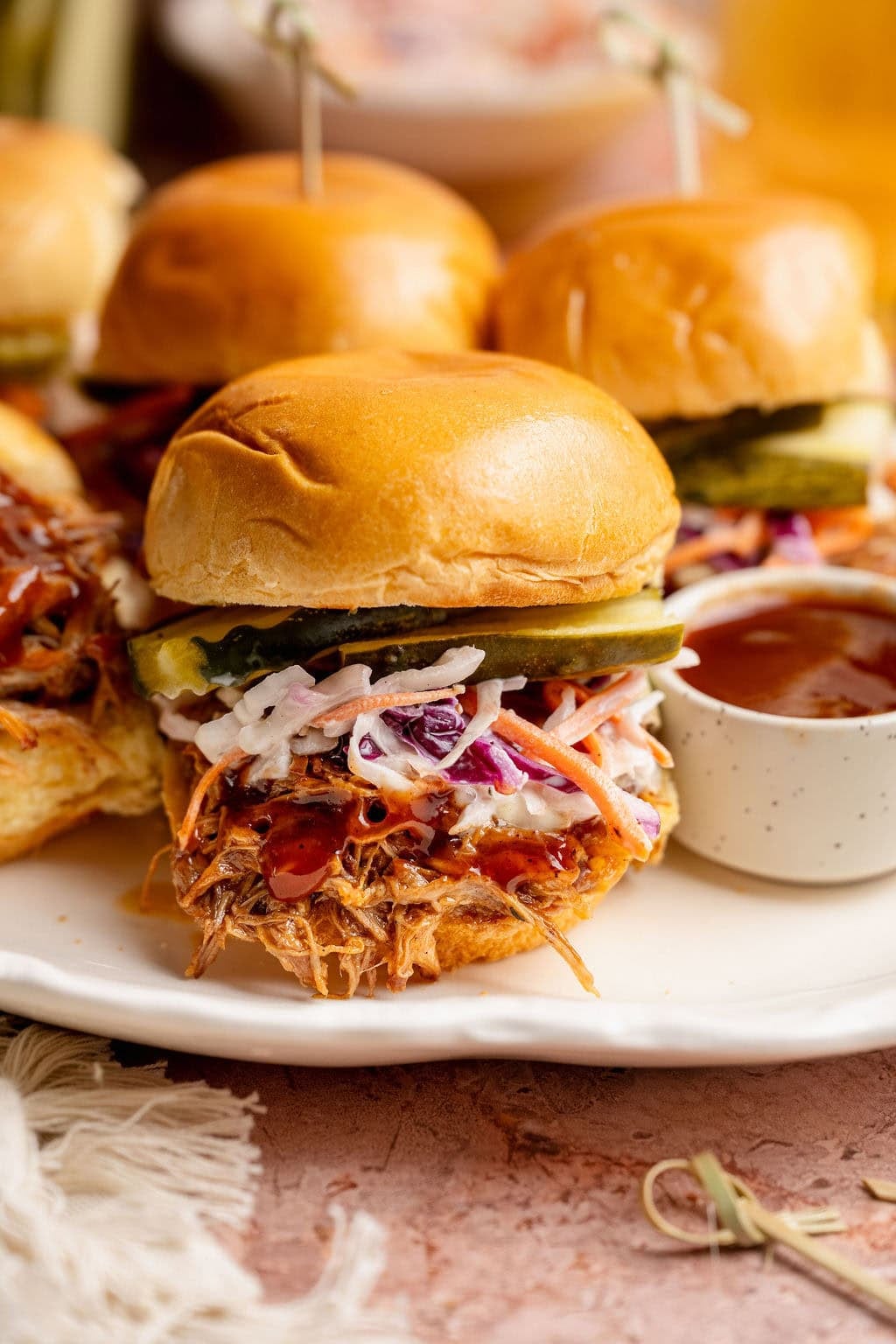 Close up view of a pork slider layered with BBQ sauce, coleslaw and sliced pickles.
