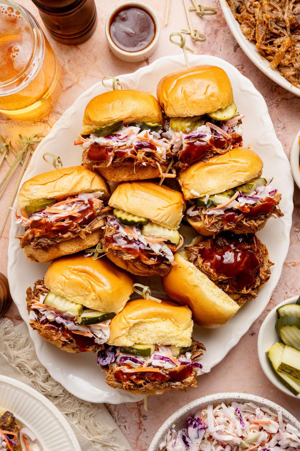 Overhead view of a platter of Pulled Pork Sliders topped with coleslaw and sliced pickles.
