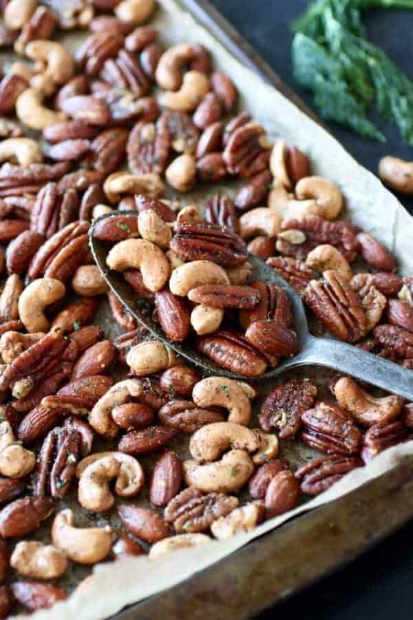 Ranch Roasted Mixed Nuts on a baking pan with a silver spoon holding a scoop of nuts also on the pan. 