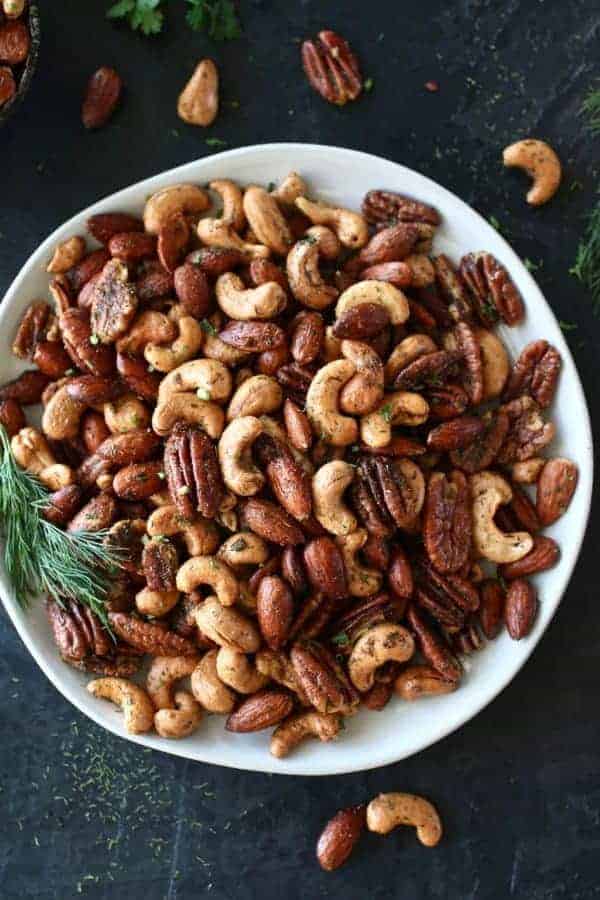Overhead photo of Ranch Roasted Mixed Nuts on a white plate with dill. Photo taken on a dark background.