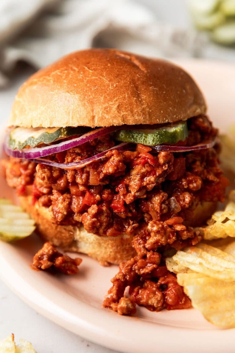 Close up view of a loaded sloppy joe on a bun topped with pickles and red onions. 
