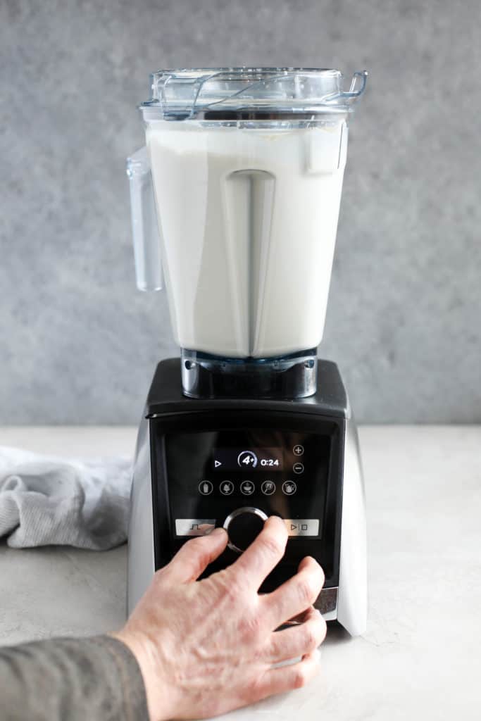 A hand turning up a blender filled with cream