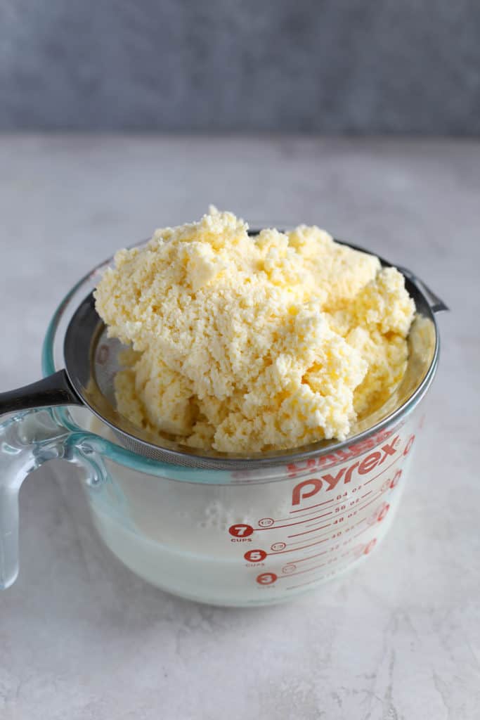 Butter in a strainer with buttermilk underneath in a glass measuring cup