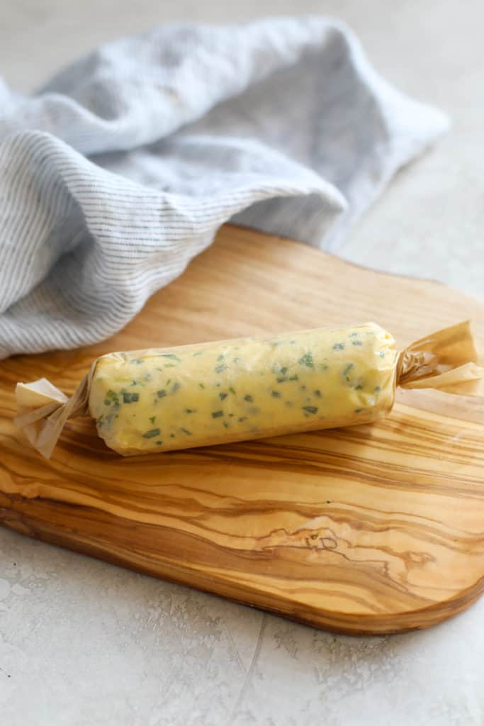 A fresh log of butter with herbs in it, wrapped in parchment paper
